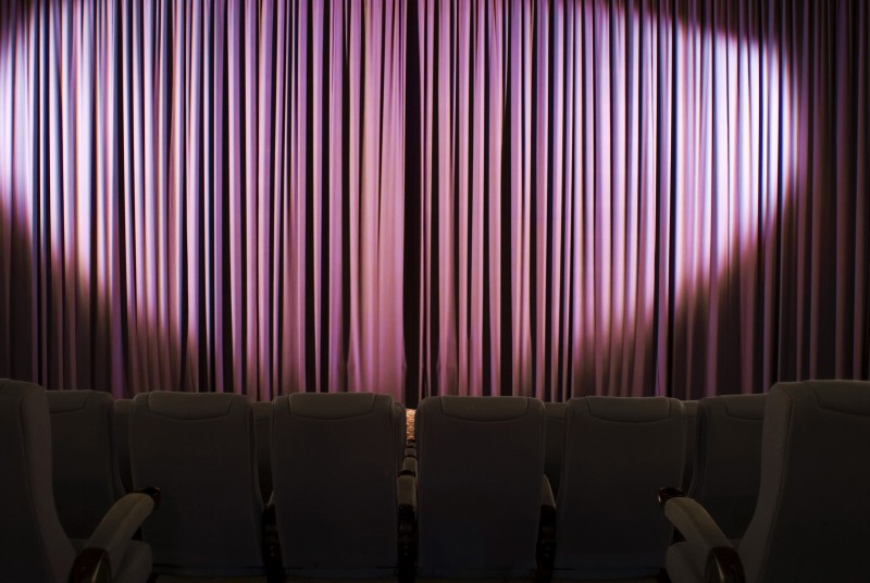 Darkened seats before a stage cutain lit by a large oval spotlight in a cinema or theatre